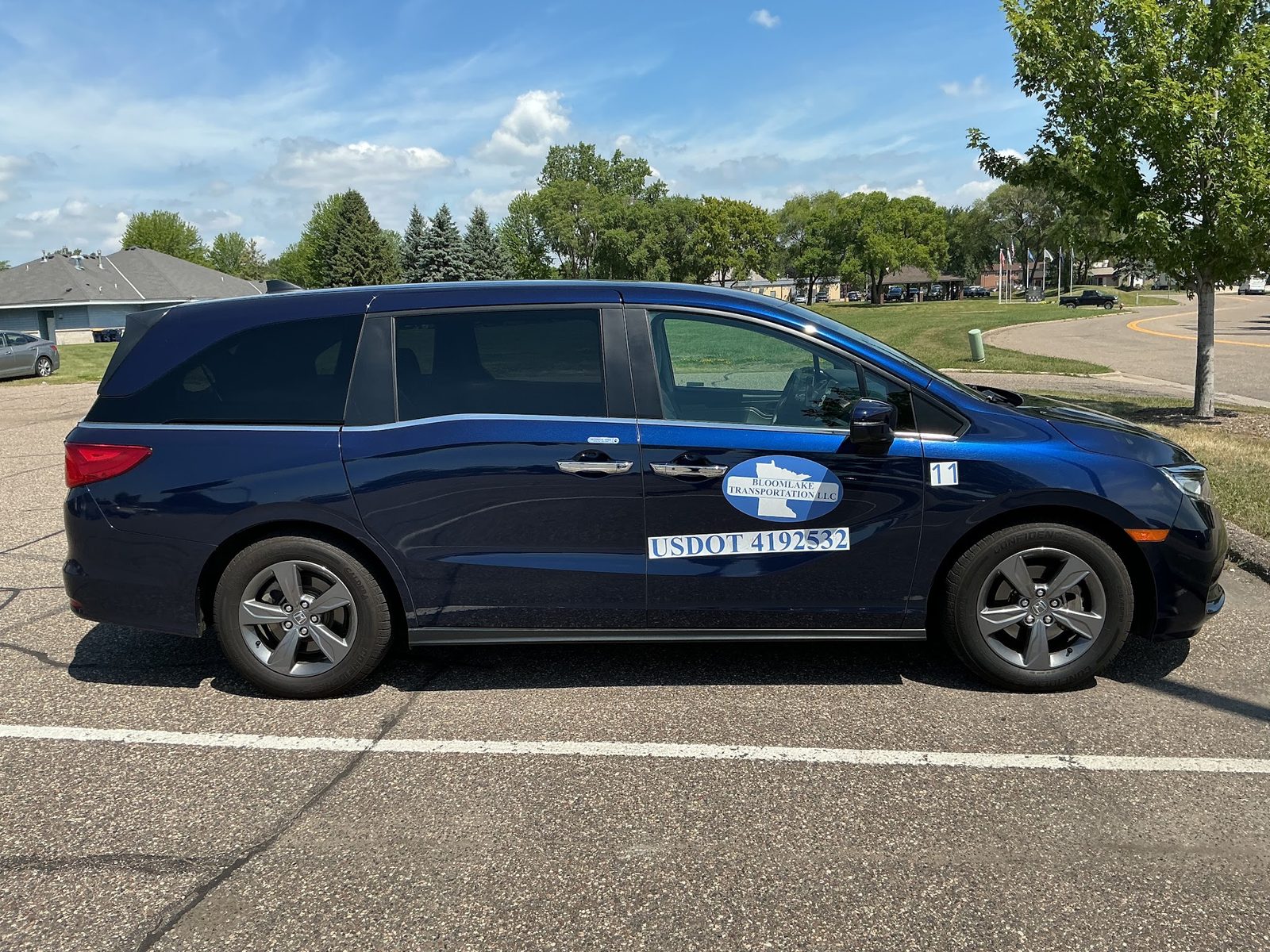 A dark blue Bloomlake Transportation minivan parked on a quiet residential street on a clear day.