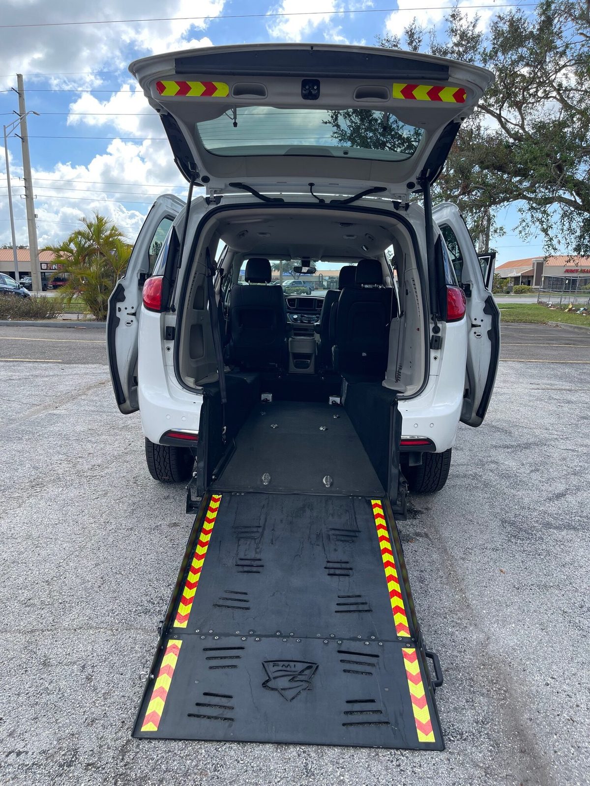 A wheelchair-accessible passenger van with its rear ramp lowered to the ground, ready for a wheelchair to be rolled aboard.